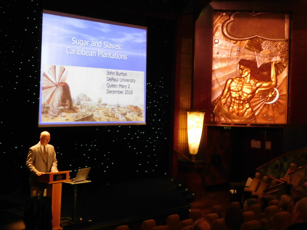 A speaker does an Insight Talk on Queen Mary 2 in Illuminations about Sugar and Slaves: Caribbean Plantations